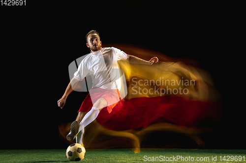 Image of Male soccer player kicking ball on dark background in mixed light