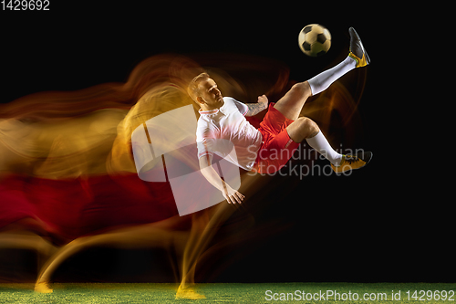 Image of Male soccer player kicking ball on dark background in mixed light