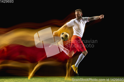 Image of Male soccer player kicking ball on dark background in mixed light