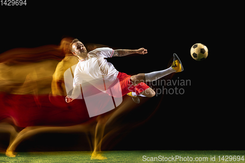 Image of Male soccer player kicking ball on dark background in mixed light