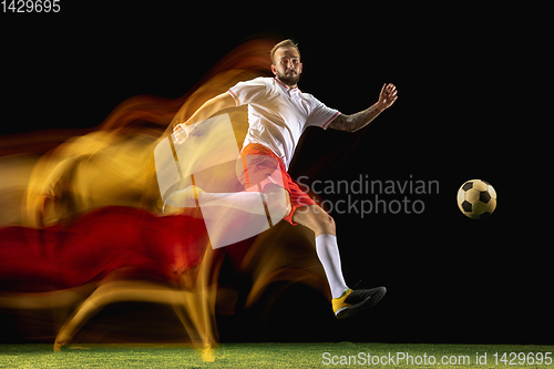 Image of Male soccer player kicking ball on dark background in mixed light