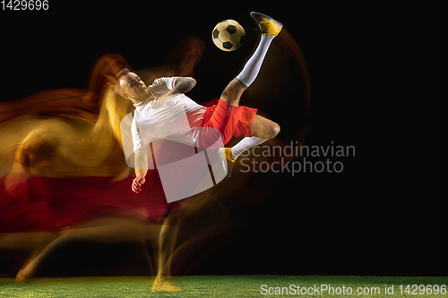 Image of Male soccer player kicking ball on dark background in mixed light