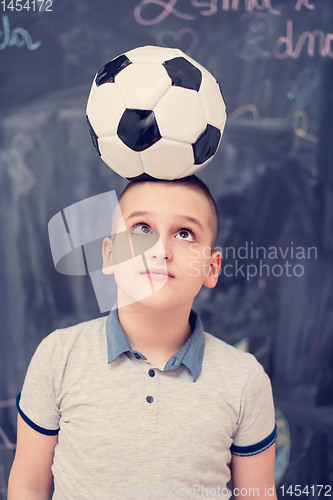 Image of happy boy holding a soccer ball on his head