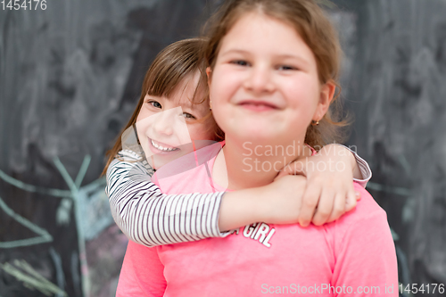 Image of little girls hugging in front of chalkboard