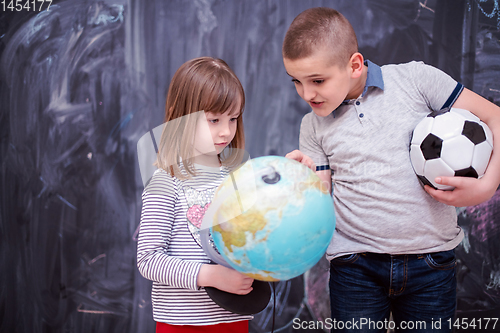 Image of boy and little girl using globe of earth in front of chalkboard