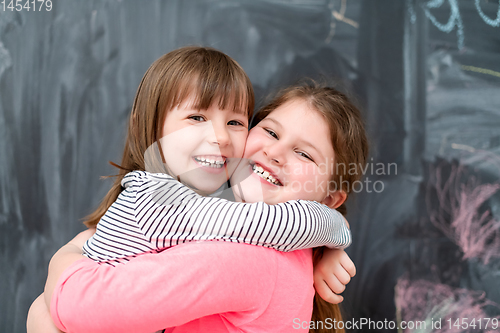 Image of little girls hugging in front of chalkboard