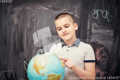 Image of boy using globe of earth in front of chalkboard