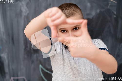 Image of happy boy making hand frame gesture in front of chalkboard