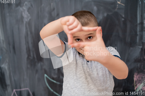 Image of happy boy making hand frame gesture in front of chalkboard