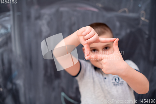 Image of happy boy making hand frame gesture in front of chalkboard