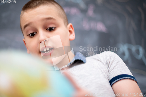 Image of boy using globe of earth in front of chalkboard