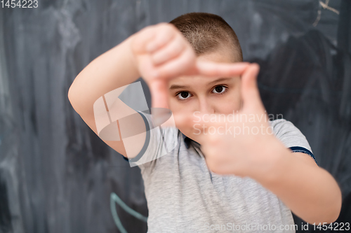 Image of happy boy making hand frame gesture in front of chalkboard