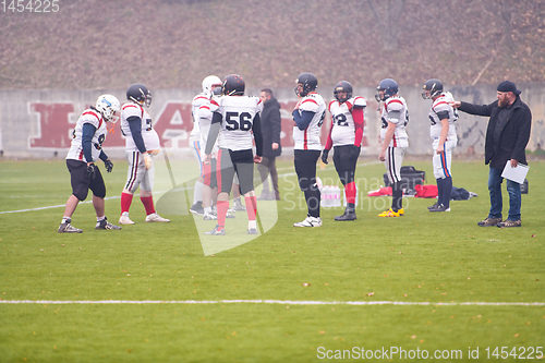 Image of american football players discussing strategy with coach