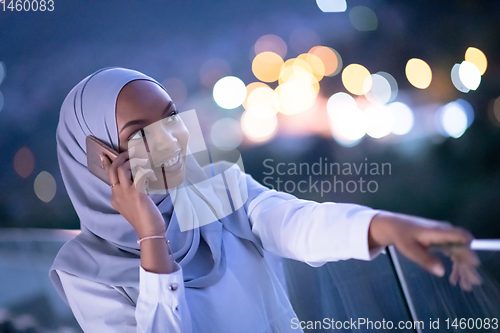 Image of Young Muslim woman on  street at night using phone