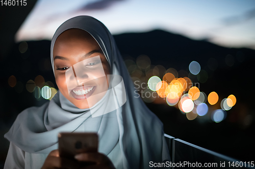 Image of Young Muslim woman on  street at night using phone