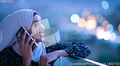 Image of Young Muslim woman on  street at night using phone