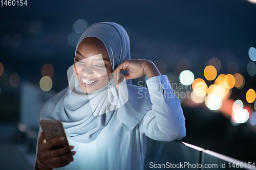 Image of Young Muslim woman on  street at night using phone