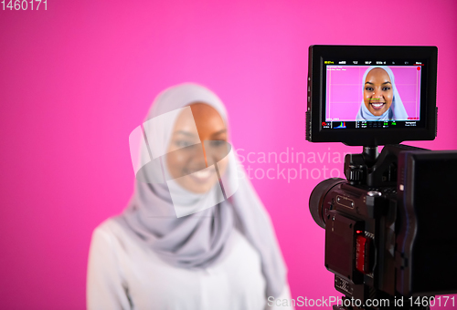 Image of videographer in pink studio recording video on professional came