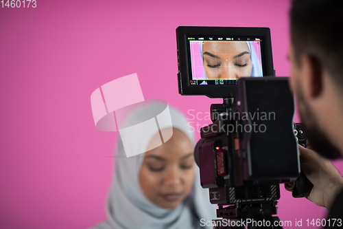 Image of videographer in pink studio recording video on professional came