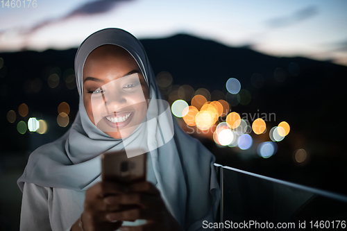 Image of Young Muslim woman on  street at night using phone