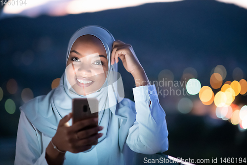 Image of Young Muslim woman on  street at night using phone