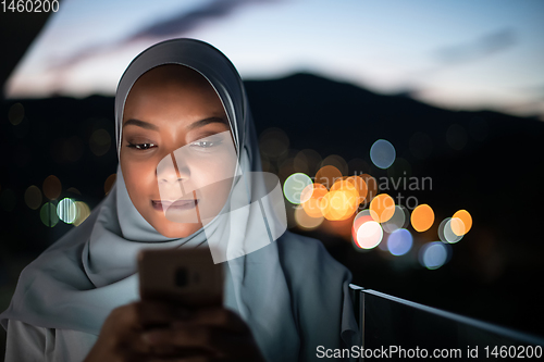 Image of Young Muslim woman on  street at night using phone