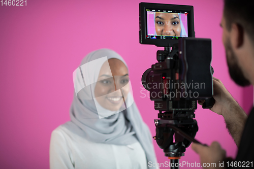 Image of videographer in pink studio recording video on professional came