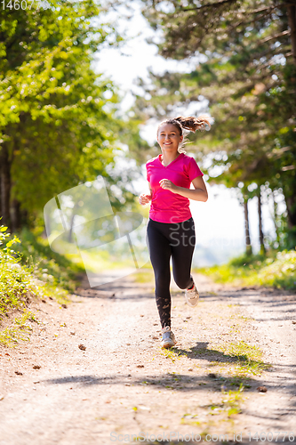 Image of young woman jogging on sunny day at nature