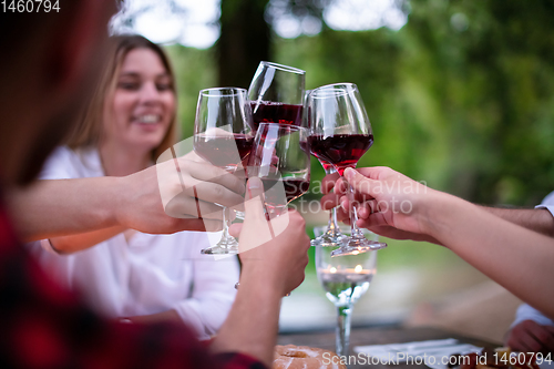 Image of happy friends toasting red wine glass during french dinner party