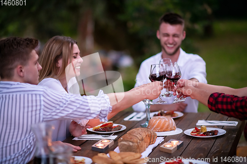 Image of happy friends toasting red wine glass during french dinner party
