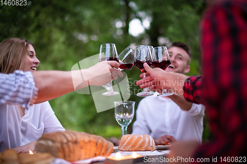 Image of happy friends toasting red wine glass during french dinner party