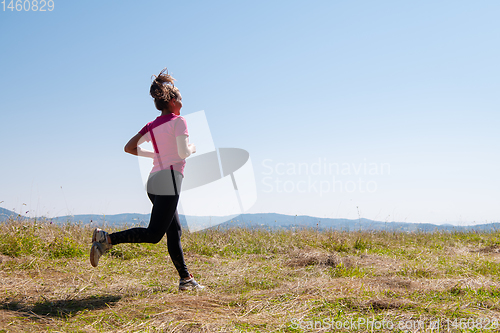 Image of young woman jogging on sunny day at summer mountain