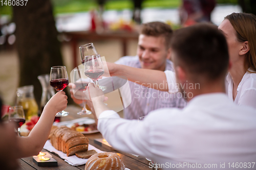 Image of happy friends toasting red wine glass during french dinner party