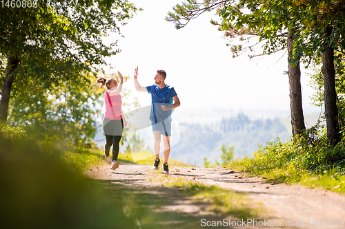 Image of jogging couple giving high five to each other on sunny day at na