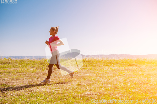 Image of young woman jogging on sunny day at summer mountain