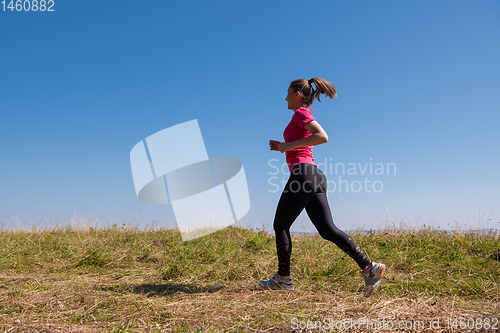 Image of young woman jogging on sunny day at summer mountain