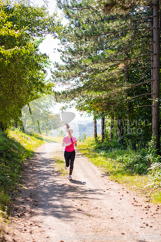 Image of young woman jogging on sunny day at nature