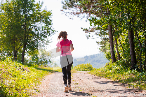 Image of young woman jogging on sunny day at nature