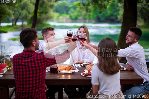 Image of happy friends toasting red wine glass during french dinner party