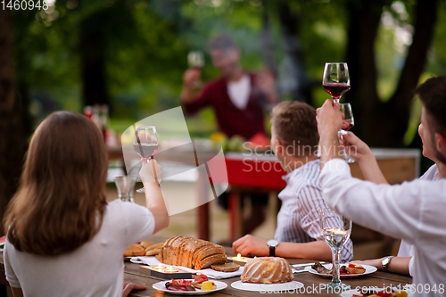 Image of happy friends toasting red wine glass during french dinner party