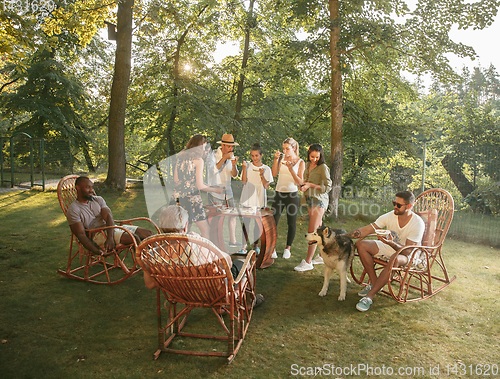 Image of Happy friends eating and drinking beers at barbecue dinner on sunset time