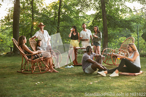 Image of Happy friends eating and drinking beers at barbecue dinner on sunset time