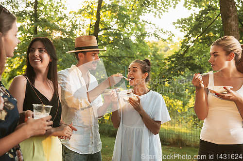 Image of Happy friends eating and drinking beers at barbecue dinner on sunset time