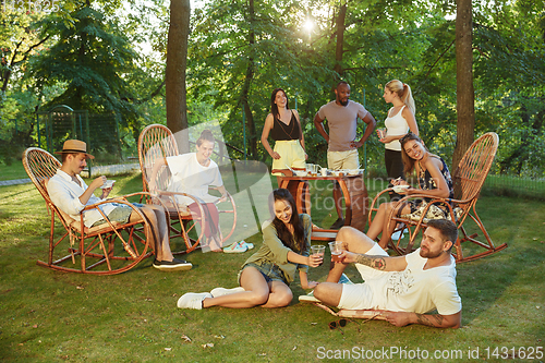 Image of Happy friends eating and drinking beers at barbecue dinner on sunset time