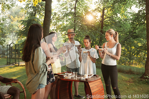 Image of Happy friends eating and drinking beers at barbecue dinner on sunset time