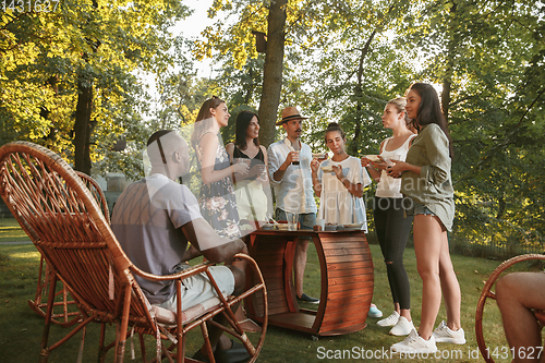 Image of Happy friends eating and drinking beers at barbecue dinner on sunset time