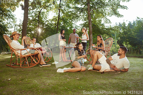 Image of Happy friends eating and drinking beers at barbecue dinner on sunset time