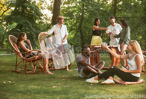 Image of Happy friends eating and drinking beers at barbecue dinner on sunset time