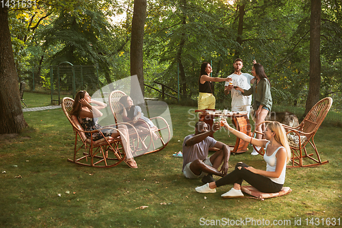 Image of Happy friends eating and drinking beers at barbecue dinner on sunset time