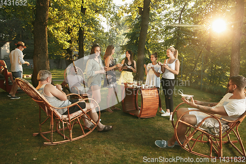 Image of Happy friends eating and drinking beers at barbecue dinner on sunset time
